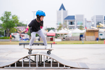 Child or kid girl playing surfskate or skateboard in skating rink or sports park at parking to wearing safety helmet elbow pads wrist and knee support - 508951049