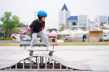 Rolgordijnen Child or kid girl playing surfskate or skateboard in skating rink or sports park at parking to wearing safety helmet elbow pads wrist and knee support © CasanoWa Stutio