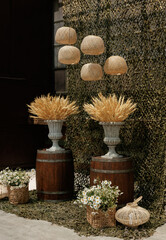 Fototapeta na wymiar Wedding ceremony in a military style with wicker lamps, baskets with daisies, vases with dry wheat on wooden barrels