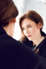 A woman stands in front of a mirror and looks away. Woman and reflection in the mirror.