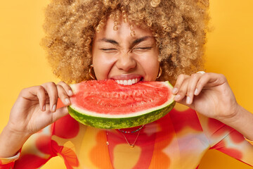 Photo of curly haired young woman eats juicy delicious watermelon bites favorite fruit keeps eyes...