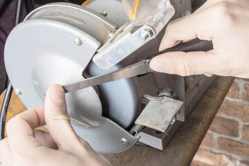 Knife sharpener and hand with blade on table, closeup