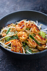 Modern style traditional stir-fried Thai phak kung with king prawns, vegetable and noodles served as close-up in a Nordic design bowl