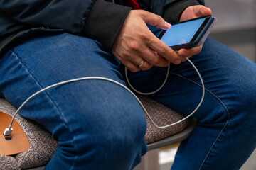 Man sitting in train and holding phone plug USB cable to free charging port