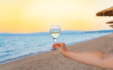 A glass of champagne or white wine in a woman's hand against the backdrop of the sea