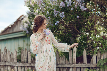 Beautiful girl in a summer dress posing against a background of flowers
