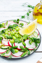 Fresh vegan salad with radish, cucumber, green pea, sunflower and soy sprouts, edamame and flax seeds. Vegetarian healthy diet food. Top view, white kitchen table