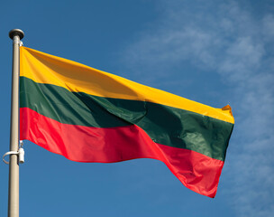 Lithuanian flag waving in the wind against sunny blue sky.