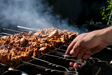 a man roasts meat on a fire. Close-up of hands and shish kebab. Cooking pork neck on the grill. Roasted carrots. Fatty food, festive food of the CIS countries. May 1, labor day. Not vegan food
