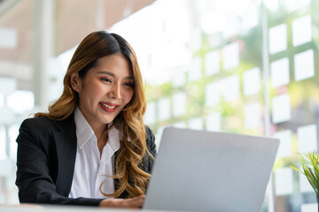 Fototapeta premium Happy young asian businesswoman sitting on her workplace in the office. Young woman working at laptop in the office.
