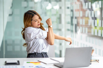 Office asian business woman stretching body for relaxing while working with laptop computer at her...