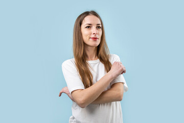 Smiling young woman in white t-shirt with arms crossed on blue background