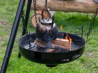 Coffee pot hanging over open fire and burning logs.