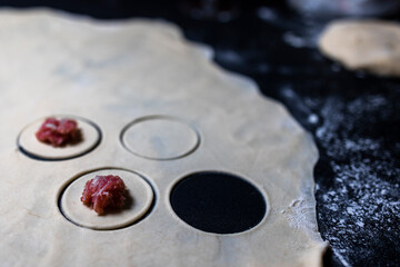 Preparation of a round shape from dough, a blank for dumplings. The minced meat is decomposed into blanks. Cooking on a black table. Flour.