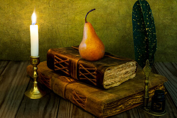 still life of antique journals, pear, quill and ink, and lit candle against a textured background