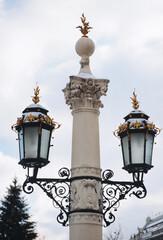 Fototapeta na wymiar Two old large black lanterns on a thick column with a capital and gilded tops in the historical center of Lviv, near the Opera and Ballet Theatre.