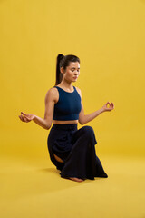 Calm female doing squatting balance pose with mudra hands, practicing yoga indoor. Front view of...
