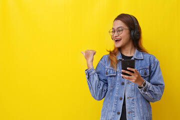Happy asian woman standing while holding a phone and presenting something sideways with copyspace