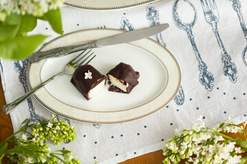 Cut into pieces cottege cheese curd or cheese cake with dark chocolate glaze and white lilac bush