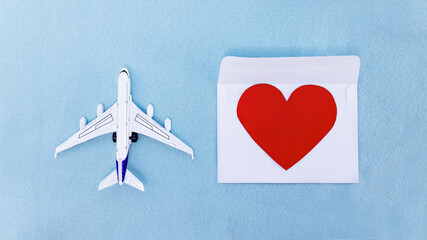 airplane symbol and
 postcard in the form of a red heart on a white envelope, blue background.
