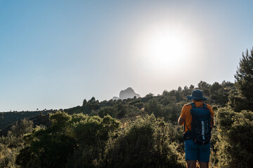 Rear view of a hiker walking through the mountains with the sun in front, on a hot summer afternoon.