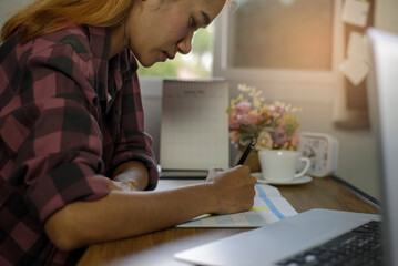Fototapeta premium Planner write meeting agenda at Calendar, work online at home. Hand of asian Woman planning daily appointment and note holiday trip schedule in diary at office desk.Calendar reminder event concept.