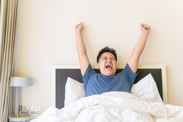 Portrait of asian obese boy awaking, wake up on the bed.