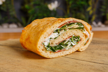 Rotolo di pizza cotto al forno ripieno di rucola, prosciutto crudo, scaglie di formaggio e stracciata di bufala servito per pranzo in una rosticceria