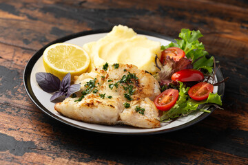 Fried cod loin fillet with mashed potato and vegetable salad served with fresh lemon
