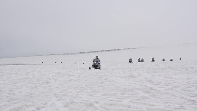 Aroup of tourists riding snowmobiles with a guide at Vatnajokull glacier in Iceland. Active sport, recreation, lifestyle.