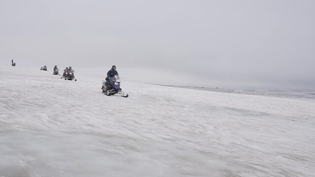Aroup of tourists riding snowmobiles with a guide at Vatnajokull glacier in Iceland. Active sport, recreation, lifestyle.