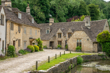honey coloured Cotswold stone houses and Bybrook river in Castle Combe Wiltshire England often...