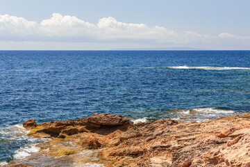 Emerald blue Mediterranean warm water gently caresses orange rocky cliff, Ibiza, Balearic Islands, Spain