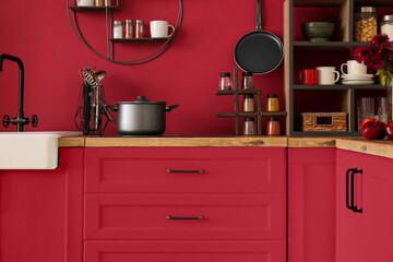 Stylish furniture with utensils and products near red wall in kitchen