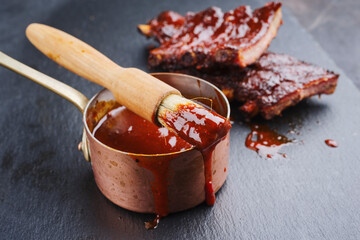 Hot and spicy barbecue sauce in a casserole as close-up with spare ribs in background