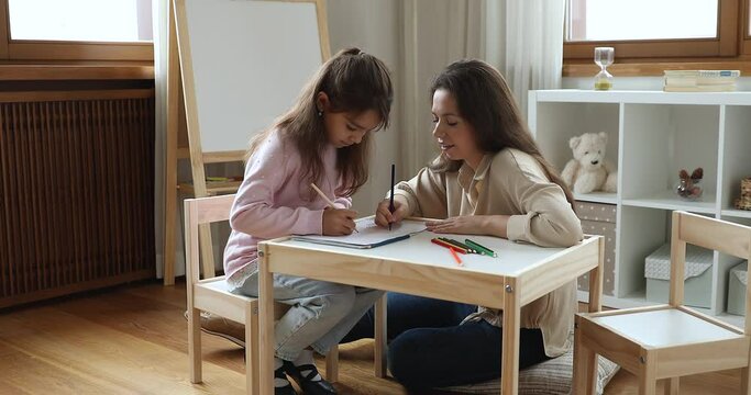 Art therapy for kids during creative process with professional, class, hobby concept. Mother spend time with little daughter sit in nursery painting with colored pencils, talking enjoy leisure at home
