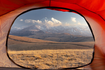 View from open door of red tent to snow-covered Mount Elbrus at sunset golden light, Caucasus Russia © Igor