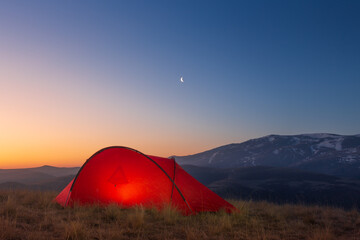 Sunrise landscape with bright tent in front of mountain ridge against colorful sky, Caucasus, Russia
