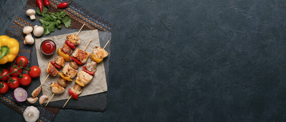 Grilled chicken skewers with vegetables and sauce on black background with space for text, top view