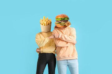 Couple with tasty french fries and burger instead of their heads bumping fists on light blue...
