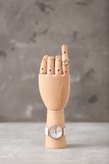 Wooden hand with wristwatch and ring on grunge background