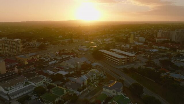 Forwards fly above large town, streets and buildings against golden sunset sky. Port Elisabeth, South Africa