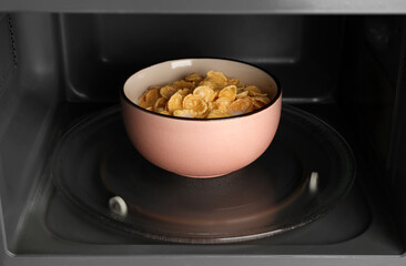 Bowl of tasty corn flakes with milk in microwave oven, closeup