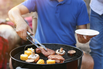 Handsome man putting grilled meat on plate at barbecue party, closeup