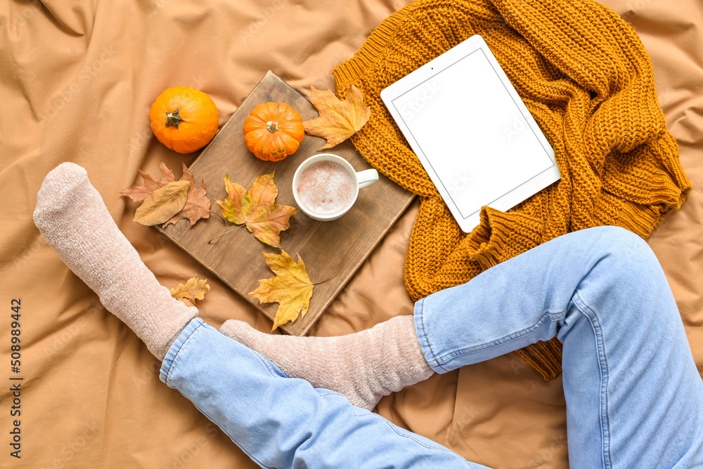 Poster woman with tablet computer and cup of tasty pumpkin coffee on bed