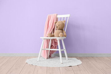 Toy bear and soft plaid on chair near violet wall in room interior