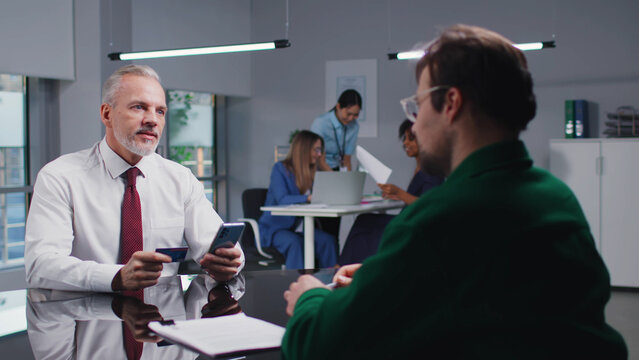 Senior businessman with smartphone and credit card make online payment in dealer office