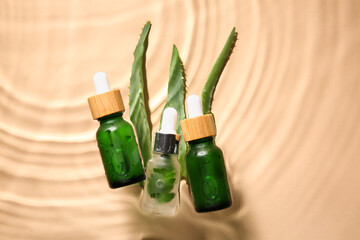 Bottles of natural serum and aloe leaves in water on color background