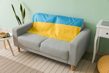 Comfortable sofa with flag of Ukraine near color wall in living room interior