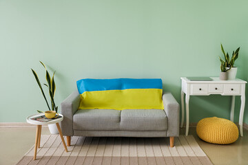 Fototapeta na wymiar Interior of living room with comfortable sofa and flag of Ukraine near color wall